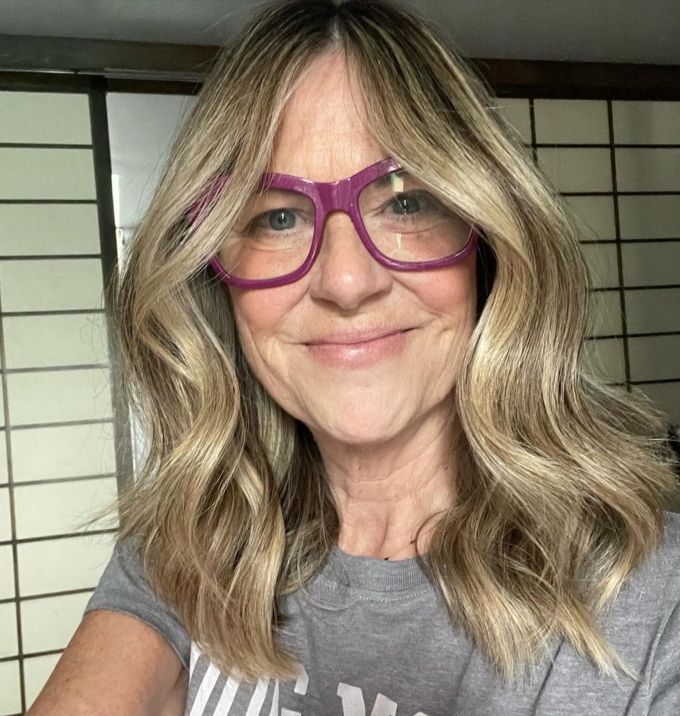 Woman smiling with long hair and glasses.