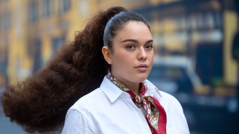 Person with long hair, wearing a scarf and white shirt.