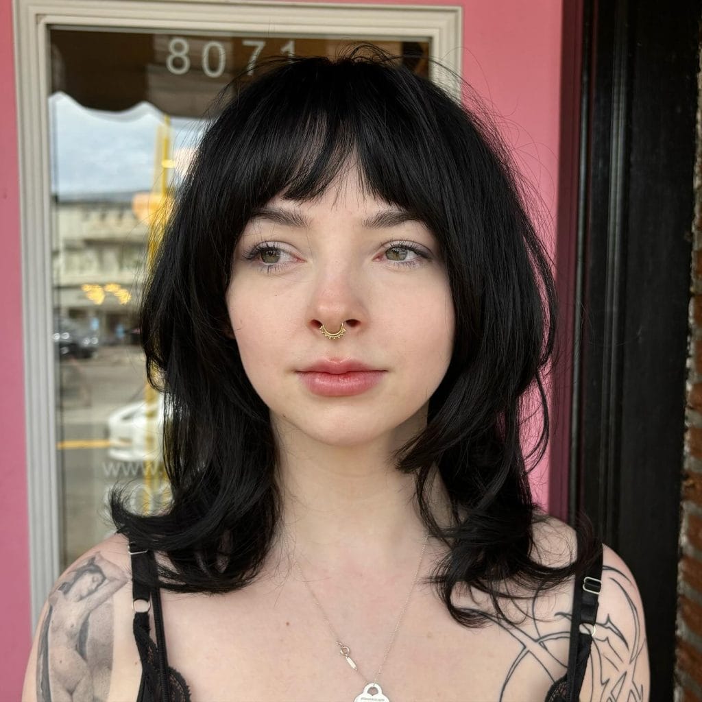 Person with black hair, tattoos, and nose ring.