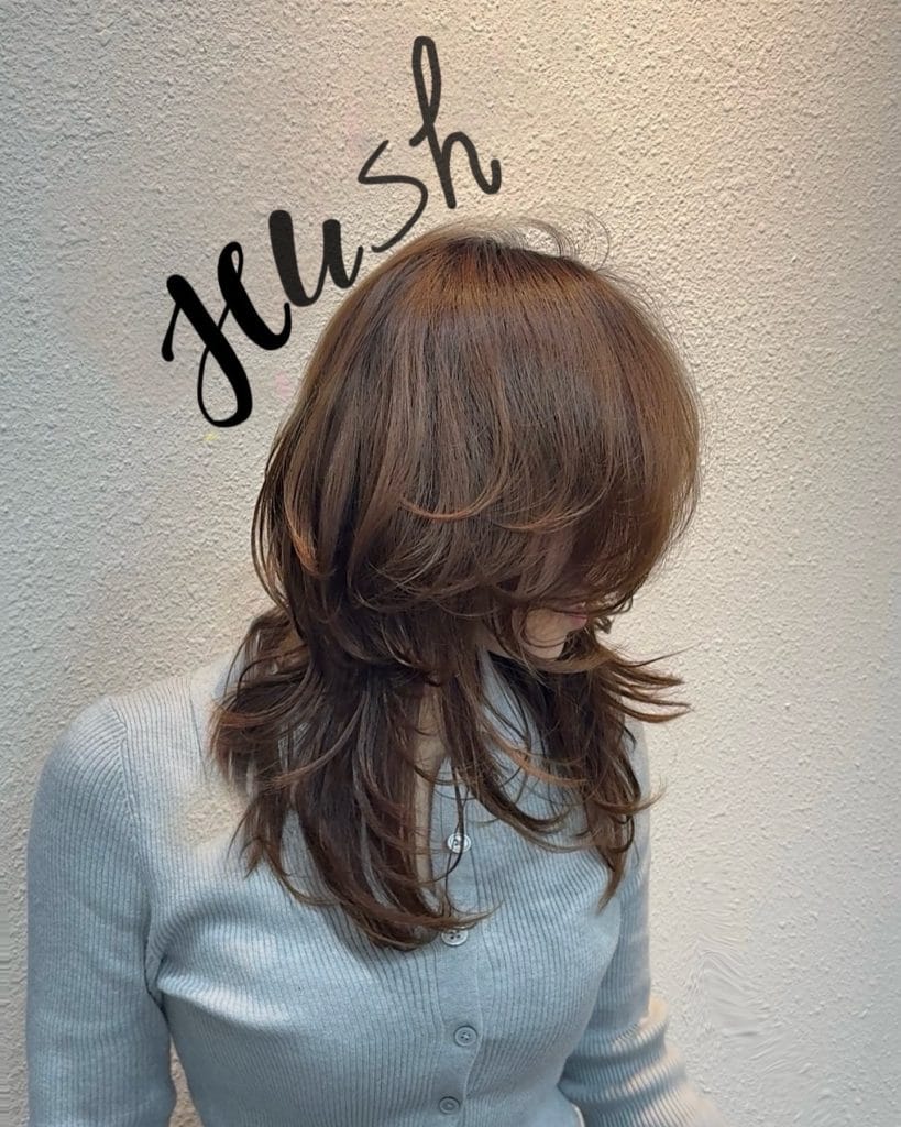 Woman with layered brown hairstyle and gray top.