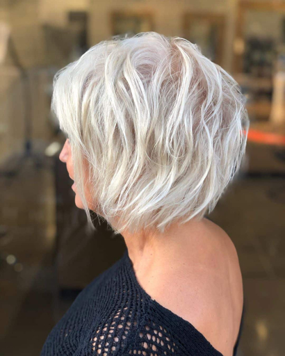 A woman with short, wavy, platinum gray hair styled in a layered bob haircut, shown in profile from the back.